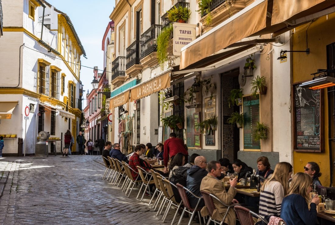 People eating and drinking at small outdoor tables on a street in Sevilla, Spain. 