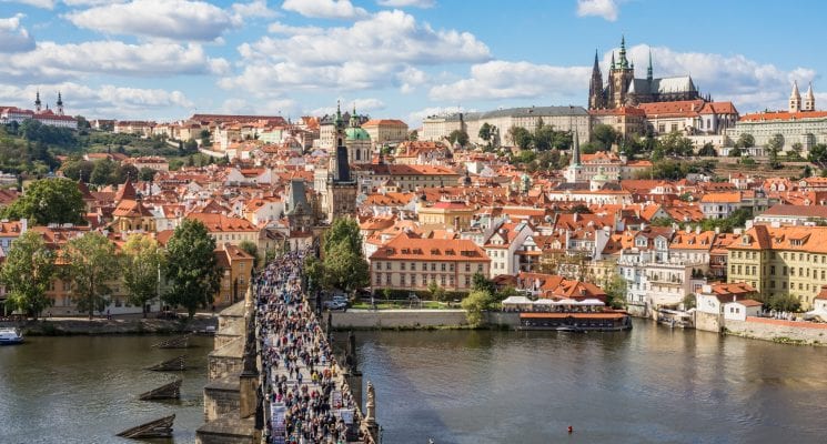 People walking across the Charles Bridge with Prague Castle in the background