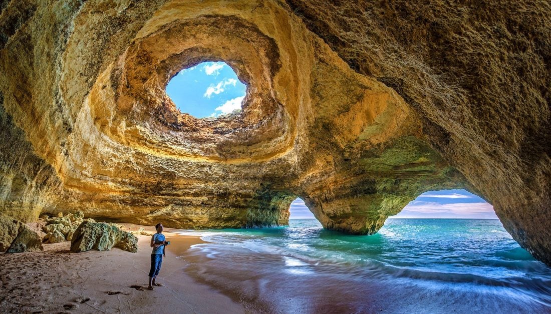 Man with camera standing by the shore of Praia de Benagil, Algarve.