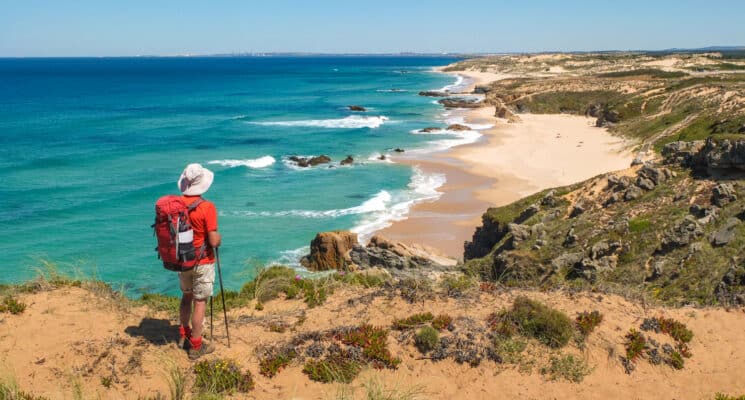 A man with a backpack enjoys the serene ocean view at Praia do Malhão, taking in the beauty of the beach.