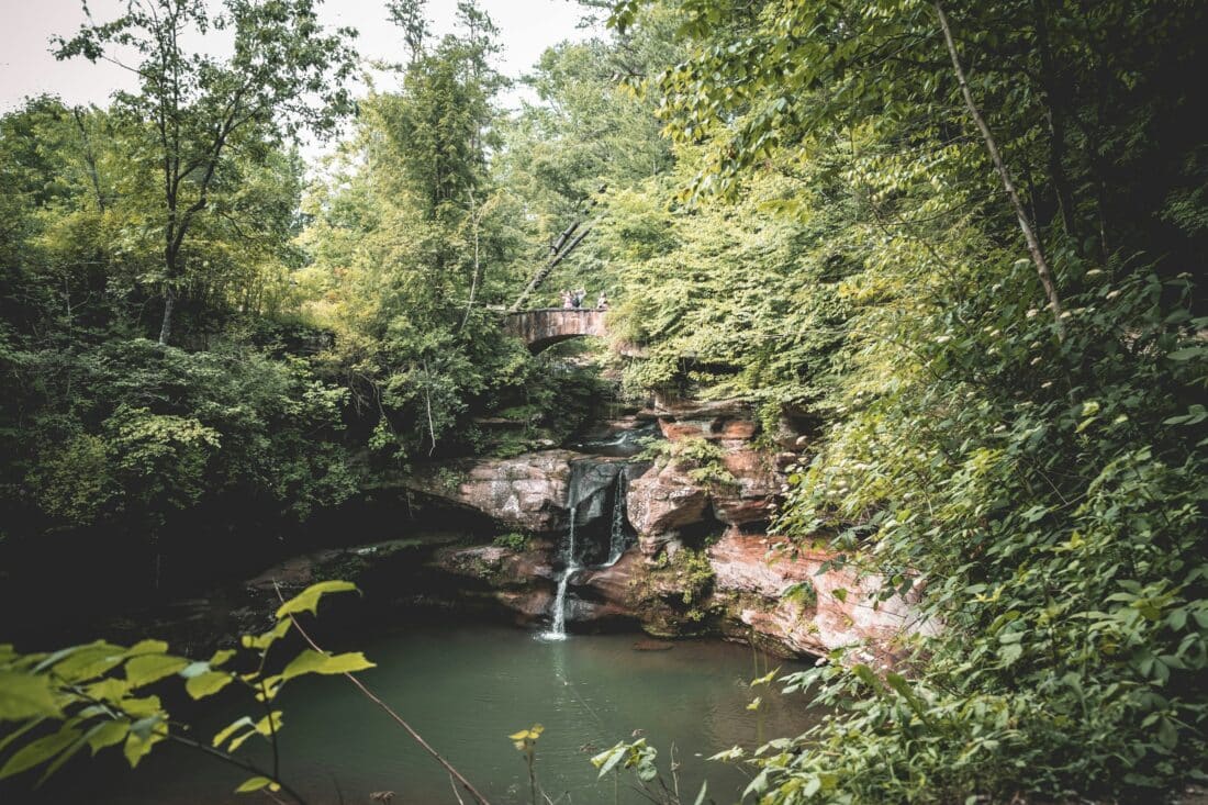 A waterfall cascading over rocks into a tranquil pool surrounded by foliage in Hocking Hills State Park, one of the best day trips from Cincinnati.