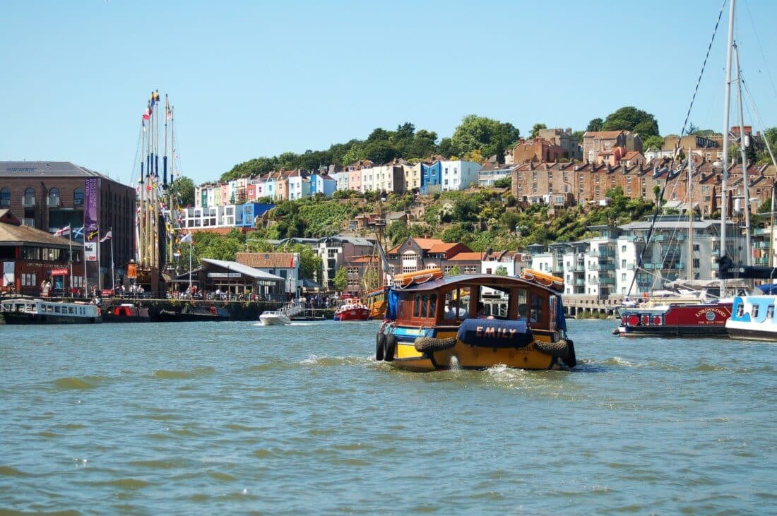 A ferry on the water in front of a colorful row of houses in Bristol, UK.